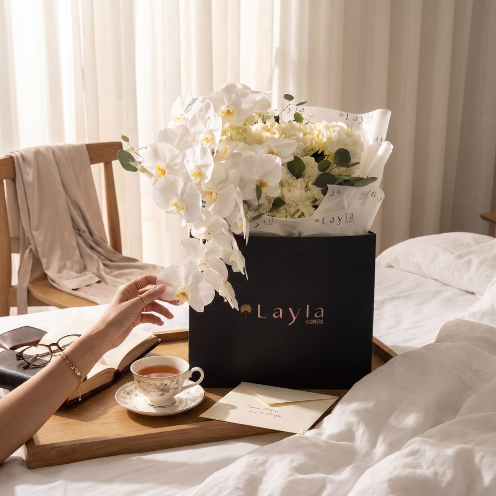 White orchids in a black Layla Flowers gift bag on a breakfast tray