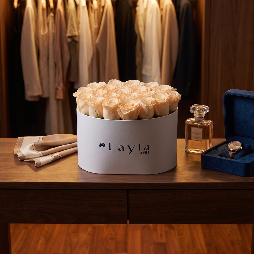 Cream roses in a white Layla Flowers hat box beside perfume and a watch