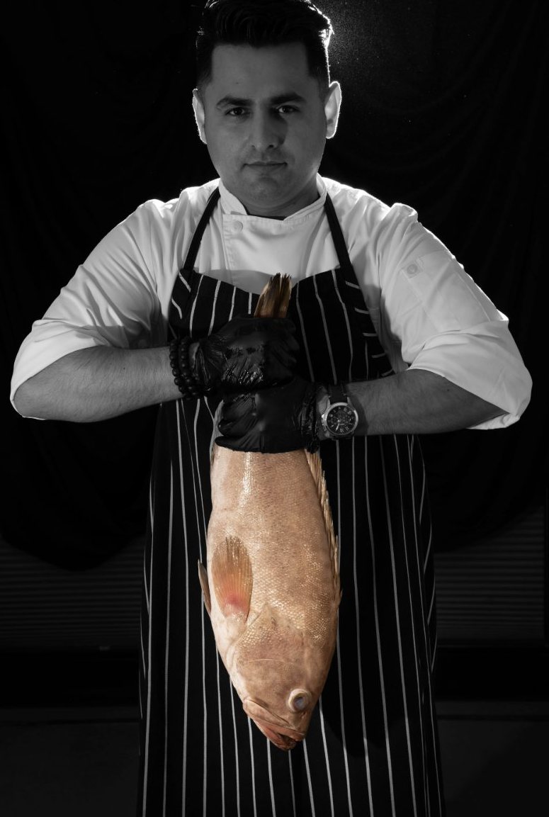 Black-and-white portrait of a chef holding a whole hammour fish