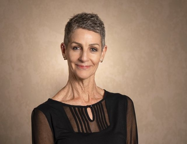 Studio headshot of a woman in a black top on a warm backdrop